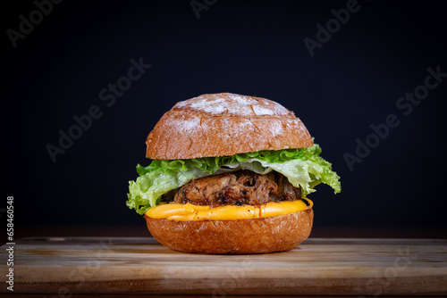 Pork sandwich with lettuce, tomato, cheddar cheese served on cutting board on a black wooden table. Craft sandwich, hand made..