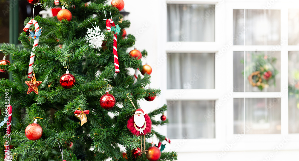 Decorate christmas tree with red balls, toys and small gift boxes, the background have white wooden window frame. Inside there are curtains decorated with Christmas decorations