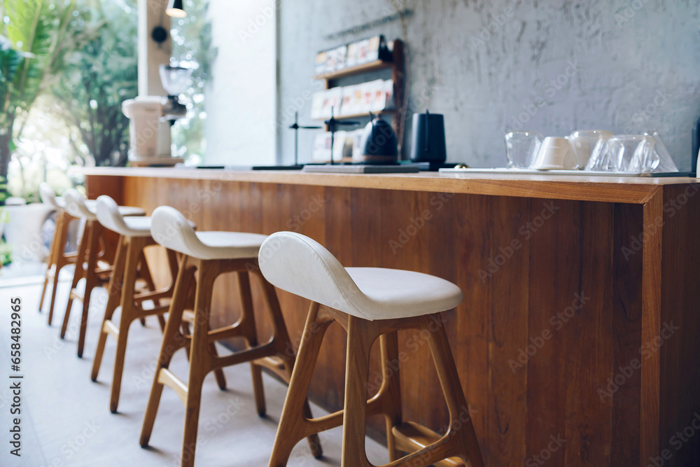 Seat and wooden counter with blur coffee equipment on counter bar and wooden shelf on rough cement wall with outdoor garden in background, Select focus at front chair
