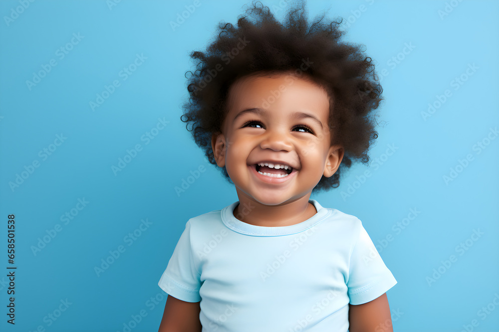 Portrait of a cute African American baby boy wearing blue tee shirt laughing on bright blue background Portrait of a cute African American baby boy wearing blue tee shirt laughing on bright blue background