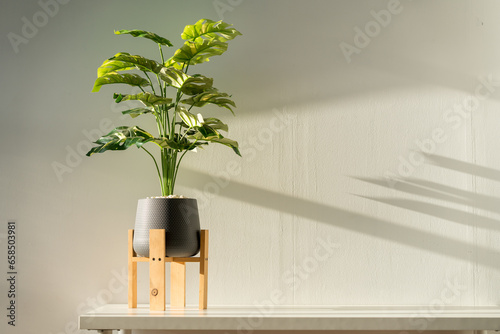 A fake Monstera plant in a gray pot sits on a white table for a simple and classy look.