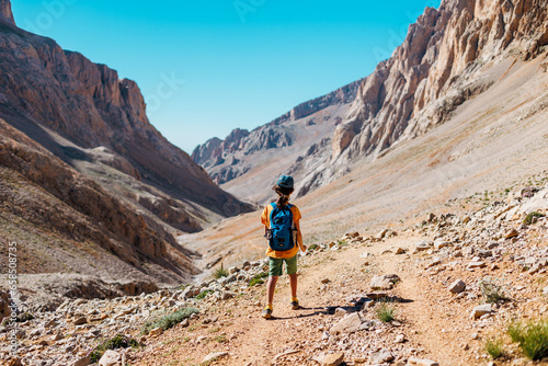 boy with a backpack walks along a mountain path. the child travels to the mountains with a backpack. mountain hike in high mountains.
