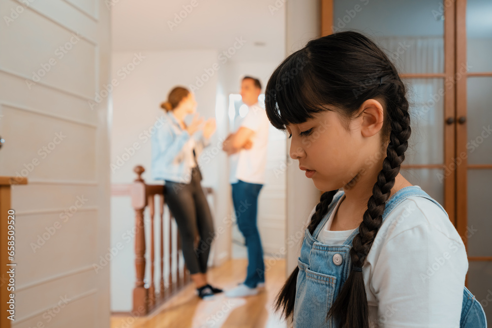 Stressed and unhappy young girl huddle in corner crying and sad while her parent arguing in background. Domestic violence at home and traumatic childhood develop to depression. Synchronos