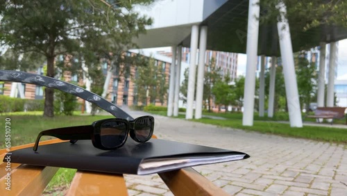 Sunglasses are lying on documents in a folder on a bench on a sunny summer day