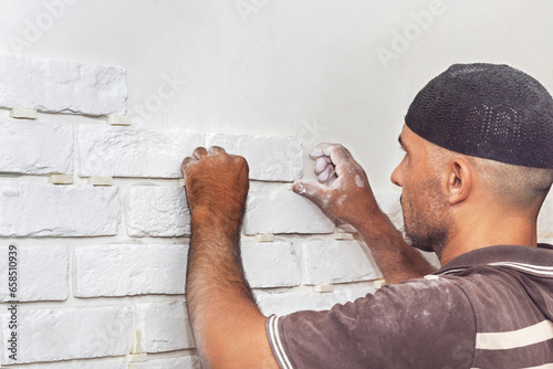 A man sticks a white decorative brick to the wall