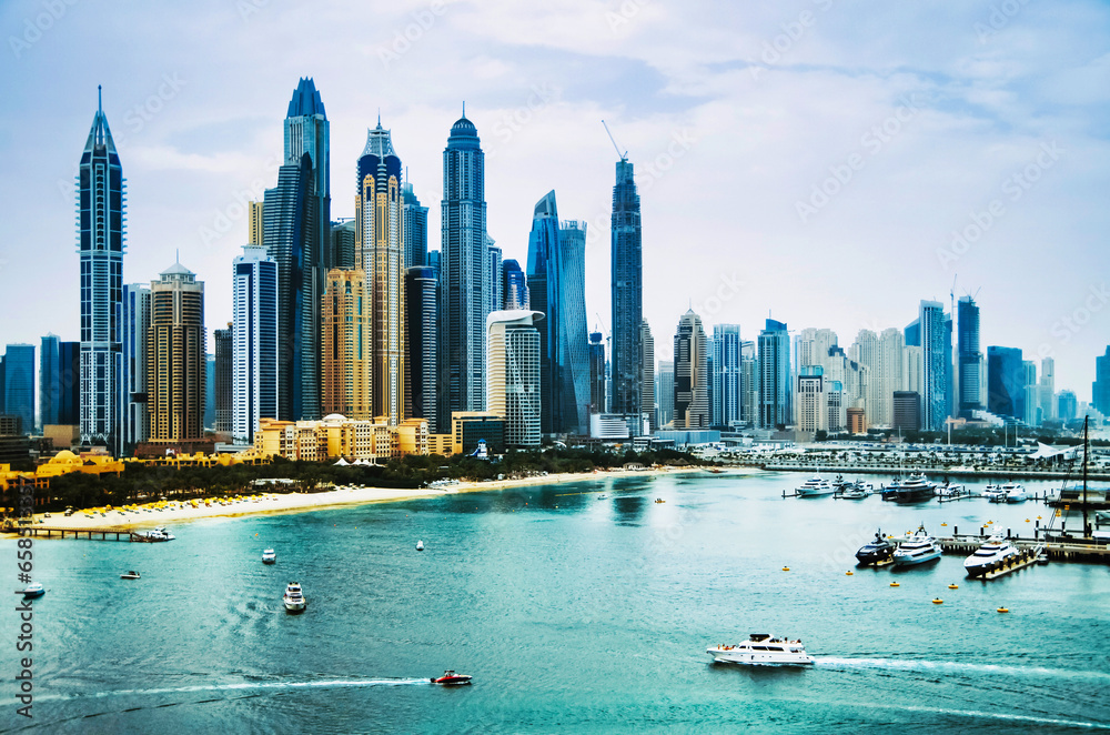 Fototapeta premium Dubai, United Arab Emirates, Dubai Marina area with famous skyscrapers, yachts and other landmarks at sunset with blue sky, view from Palm Jumeirah island