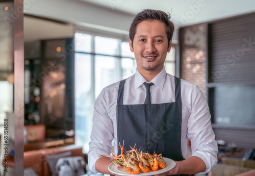 Asian man waiter working and carry and serve dish of sea food in restaurant