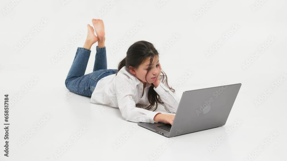 Cute, happy girl studying online using a laptop. Concept of a happy child studying online on a light background. Cute, happy girl studying online using a laptop. Concept of a happy child studying online on a light background.