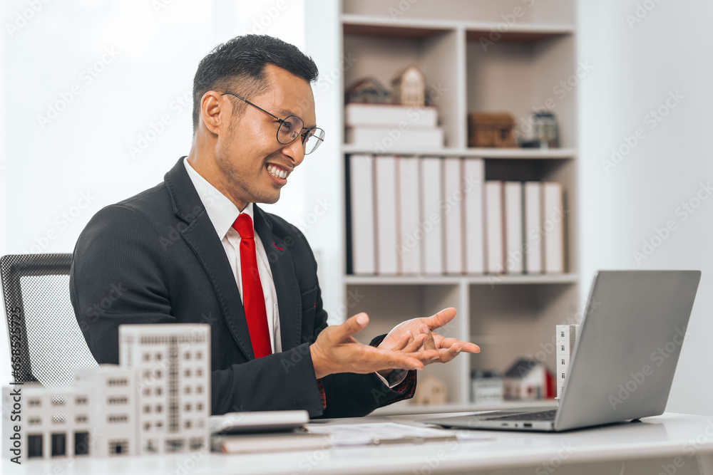 Agent presents contracts for property purchase or lease. Businessman asian indian people showcases miniature model home, signifying secure property insurance. Desk scene in a home sales office. Agent presents contracts for property purchase or lease. Businessman asian indian people showcases miniature model home, signifying secure property insurance. Desk scene in a home sales office.