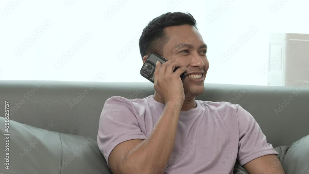 Asian indian people man and texting on cellphone in living room for online mobile app while sitting on sofa. Asian indian people man and texting on cellphone in living room for online mobile app while sitting on sofa.