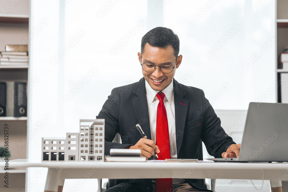 Agent presents contracts for property purchase or lease. Businessman asian indian people showcases miniature model home, signifying secure property insurance. Desk scene in a home sales office. Agent presents contracts for property purchase or lease. Businessman asian indian people showcases miniature model home, signifying secure property insurance. Desk scene in a home sales office.
