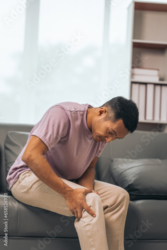 Middle-aged Asian Indian man with knee pain sitting on the sofa © NanSan