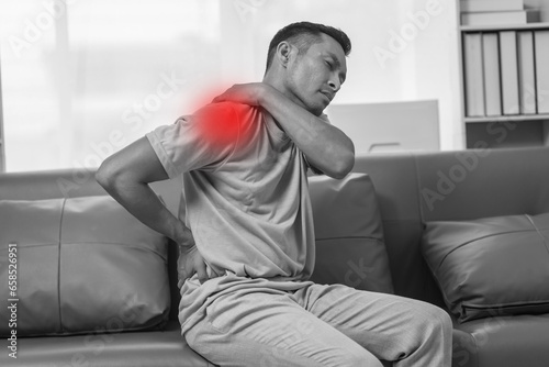 Middle-aged Asian Indian man suffering from back pain, spine and neck pain. sitting on the sofa