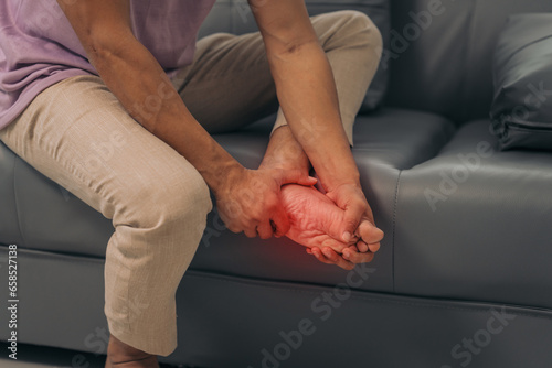 Middle-aged Asian Indian man with ankle disease, plantar pain, sitting on the sofa. © NanSan