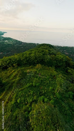 Vertical video. Aerial dive view speed flight over mountain ridge green plant sea ocean lagoon evening landscape. FPV sport drone shot picturesque Asian natural geology formation cliff rock seascape