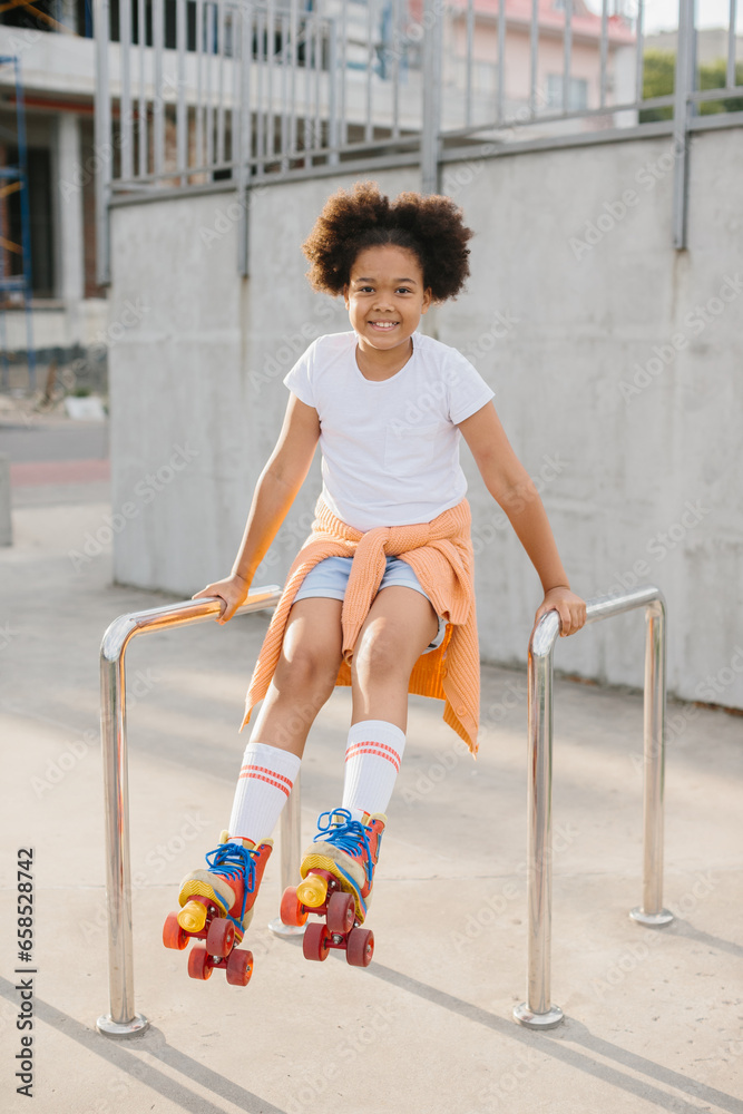 Fototapeta premium Cute young girl in roller skates having fun outdoors. The girl smiles looking at the camera.
