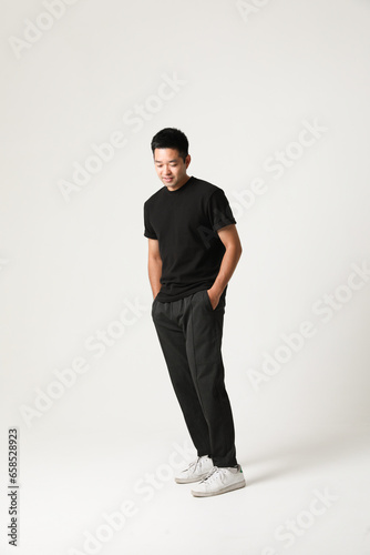Smiling young Asian man in black casual clothing posing indoor. Vertical.