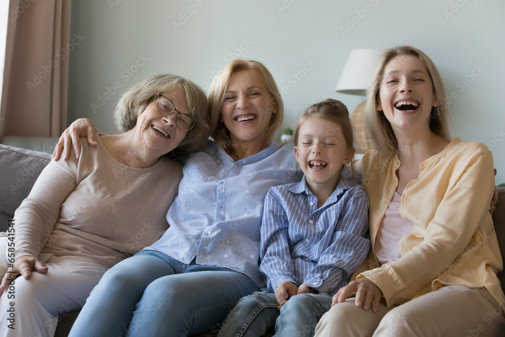 Happy excited girls and women of four family generations sitting on couch close together, hugging, laughing, smiling, looking at camera, enjoying meeting, leisure time, mothers day celebration