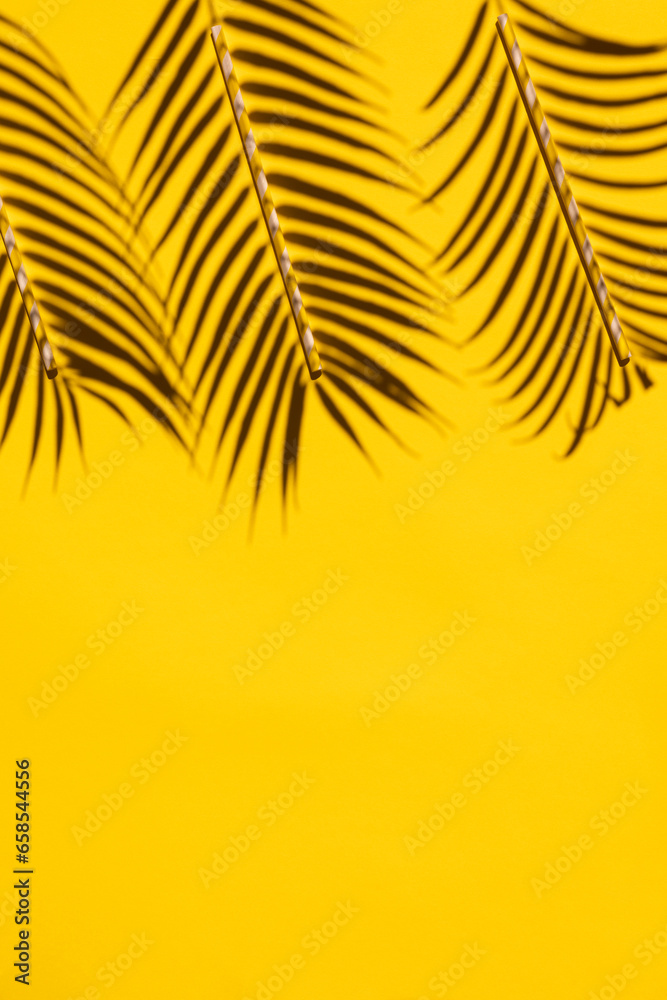 Fototapeta premium Top View of Tropical Palm Leaves Shadow and Straws on Bright Yellow Background: A Minimalistic Vertical Summer Vacation Concept Flat Lay with Creative Copy Space