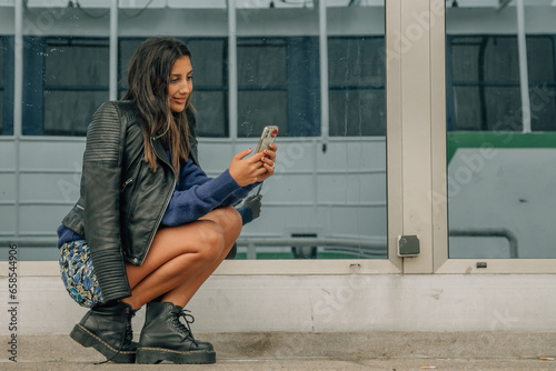 Fotografie young latin hispanic woman using phone crouching on the street