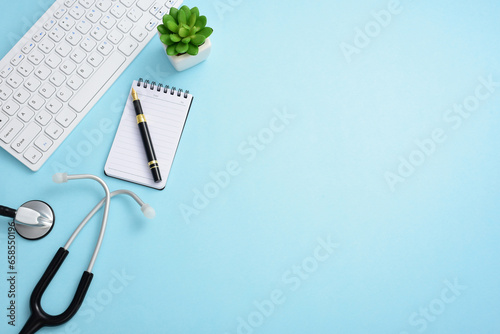 Stethoscope, computer keyboard, pen, note pad, and greenery on a blue background photo