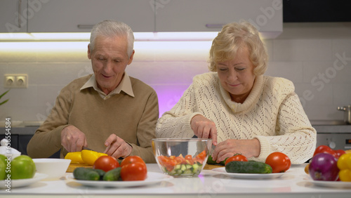Smiling senior woman and man cutting fresh vegetables in the kitchen, living a healthy lifestyle