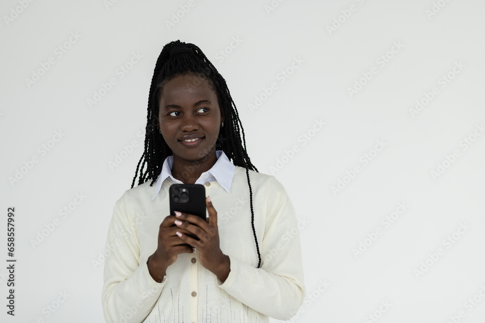 Smiling african woman using mobile phone, holding telephone and looking happy, standing over white background Smiling african woman using mobile phone, holding telephone and looking happy, standing over white background