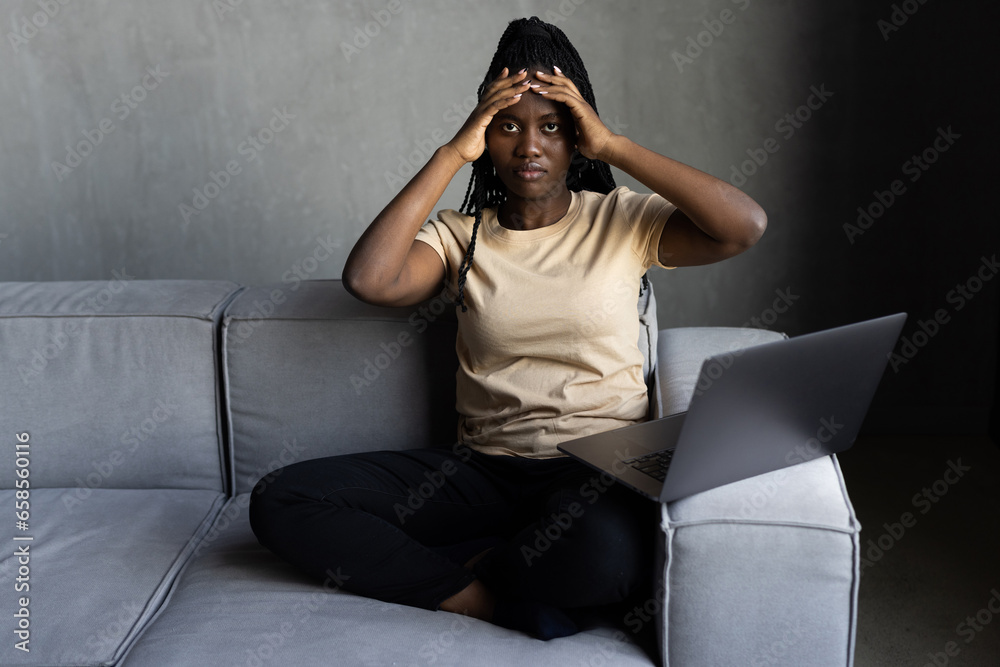 African woman using laptop at home with hand on head, headache because stress. suffering migraine. African woman using laptop at home with hand on head, headache because stress. suffering migraine.