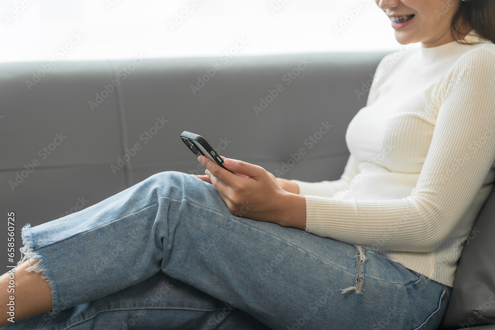 Asian woman with braces sits online shopping on sofa with laptop. mobile phone and credit card in hand Asian woman with braces sits online shopping on sofa with laptop. mobile phone and credit card in hand