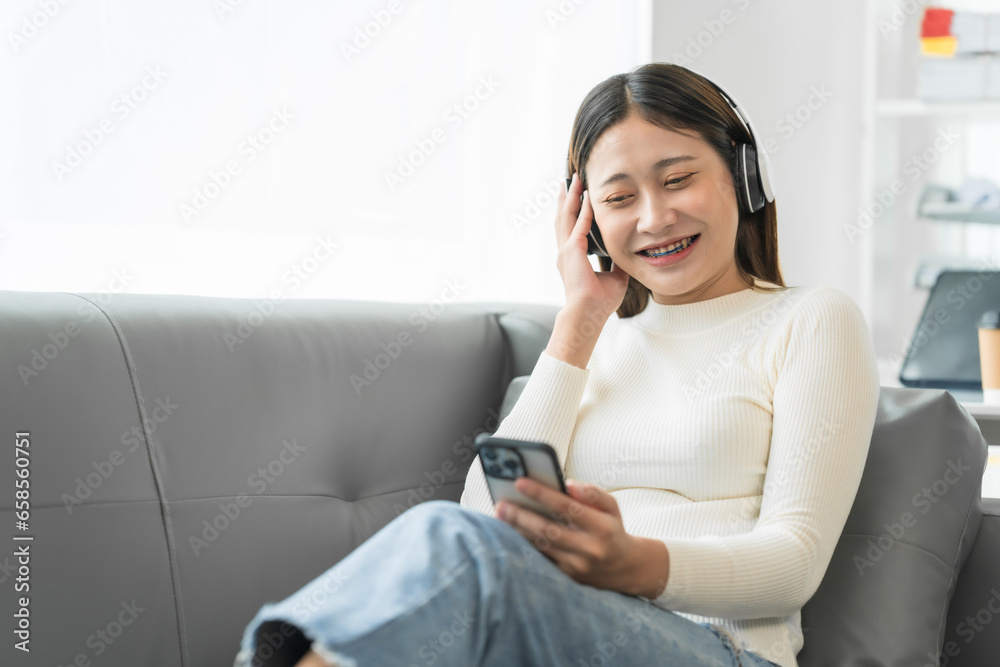 Asian woman with braces sits online shopping on sofa with laptop. mobile phone and credit card in hand Asian woman with braces sits online shopping on sofa with laptop. mobile phone and credit card in hand