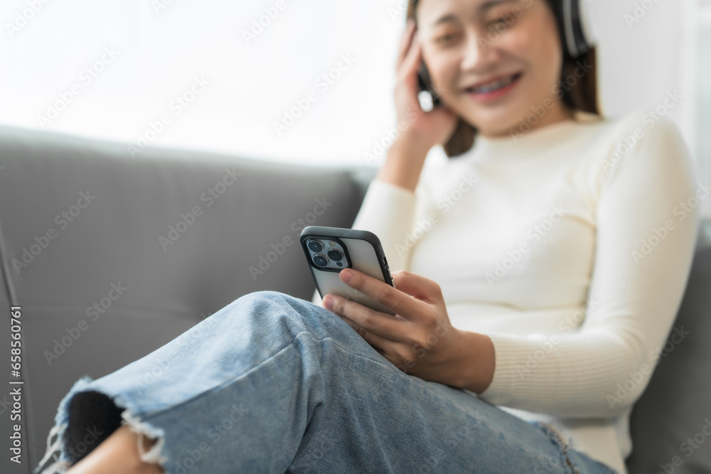 Asian woman with braces sits online shopping on sofa with laptop. mobile phone and credit card in hand