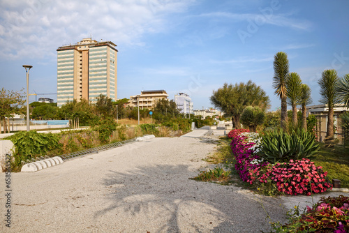 Fototapeta Naklejka Na Ścianę i Meble -  Milano Marittima, Cervia, Ravenna, Emilia Romagna: waterfront promenade on the Adriatic Sea coast with bathing establishments and in the background the skyscraper, the second one built in Italy