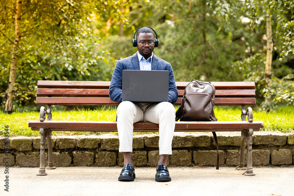 Man with headphones and laptop sitting in the park and working outside the office. Man with headphones and laptop sitting in the park and working outside the office.