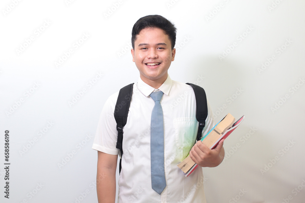 Indonesian senior high school student wearing white shirt uniform with gray tie holding some books, smiling and looking at camera. Isolated image on white background Indonesian senior high school student wearing white shirt uniform with gray tie holding some books, smiling and looking at camera. Isolated image on white background