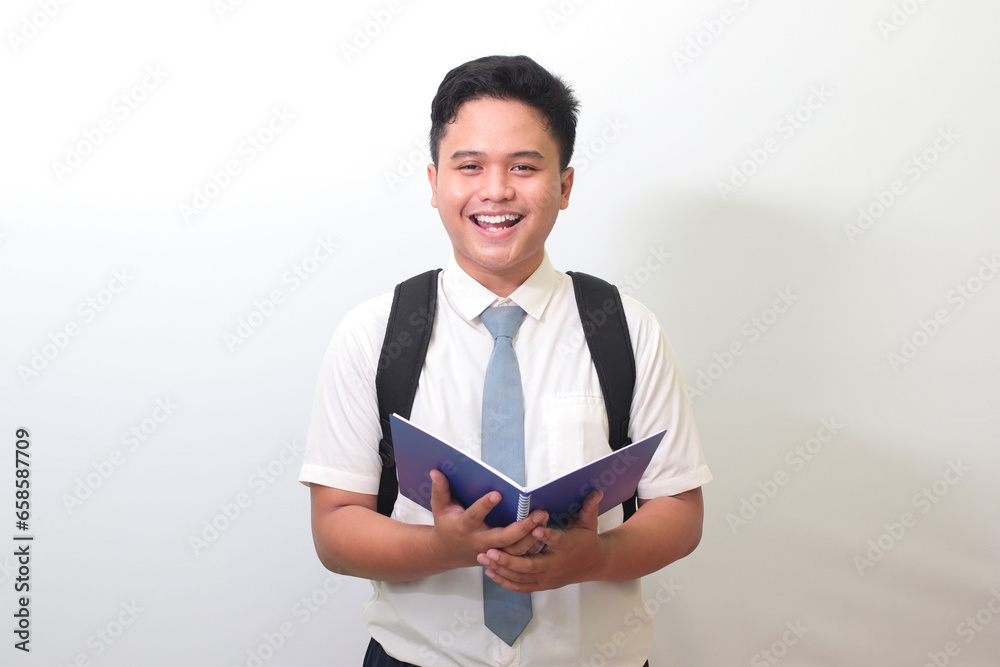 Indonesian senior high school student wearing white shirt uniform with gray tie holding a note book and smiling looking at camera. Isolated image on white background Indonesian senior high school student wearing white shirt uniform with gray tie holding a note book and smiling looking at camera. Isolated image on white background
