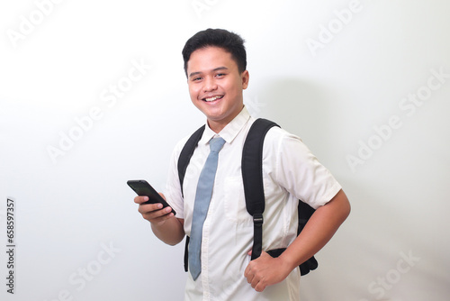 Indonesian senior high school student wearing white shirt uniform with gray tie showing shocked face expression while holding a mobile phone. Isolated image on white background