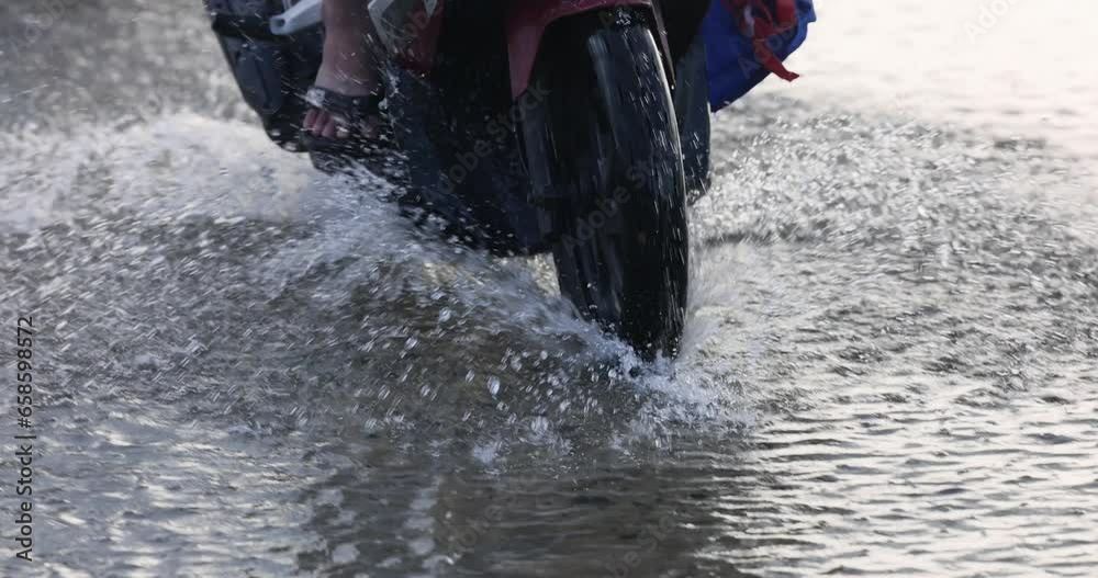 The scooter is moving along a flooded road. The scooter's wheel