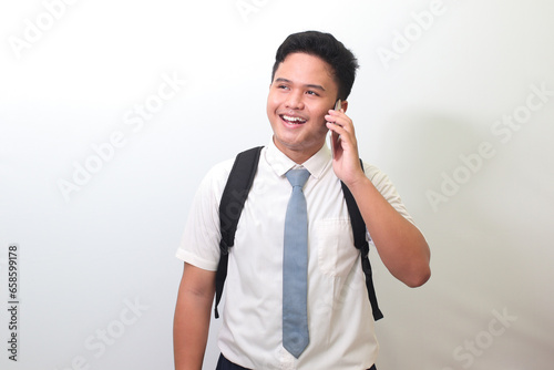 Indonesian senior high school student wearing white shirt uniform with gray tie looking up while having conversation on phone call. Isolated image on white background photo
