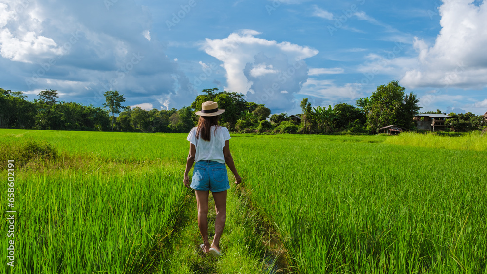 Asian woman on vacation at a small homestay at the farm with a green rice paddy field in Central Thailand
