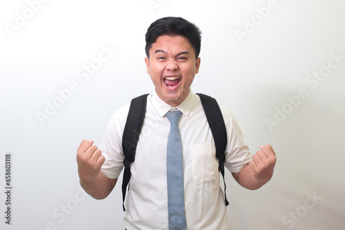 Indonesian senior high school student wearing white shirt uniform with gray tie raising his fist, celebrating success. Winning a competition concept. Isolated image on white background photo
