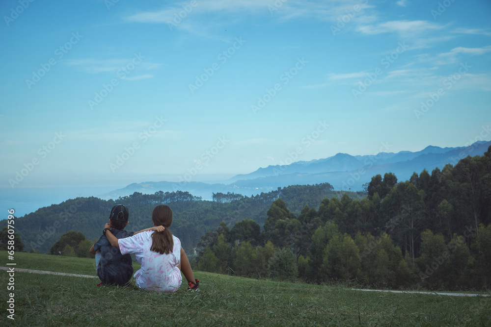 A couple of brothers hugging each other contemplate a beautiful green mountain landscape and coastal cliffs in the background A couple of brothers hugging each other contemplate a beautiful green mountain landscape and coastal cliffs in the background