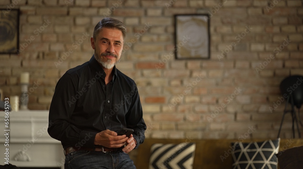 Portrait of happy, confident older man at home using phone, smiling. Mature age, middle age, mid adult casual guy in 50s, bearded, gray hair. Portrait of happy, confident older man at home using phone, smiling. Mature age, middle age, mid adult casual guy in 50s, bearded, gray hair.