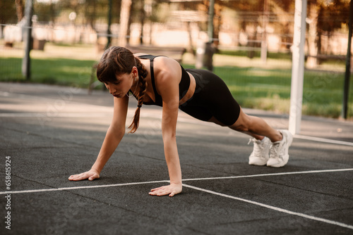 A young female trainer performs a fitness compression exercise. The girl is working out outdoors. Healthy lifestyle.