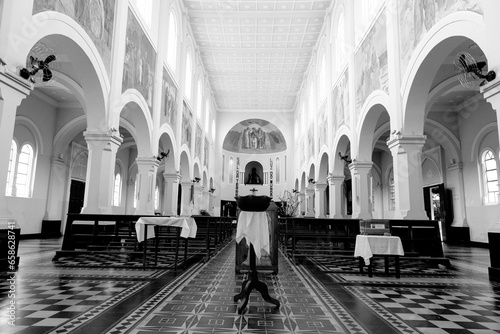 Interior de igreja católica de arquitetura clássica com arco e bancos de madeira.  photo