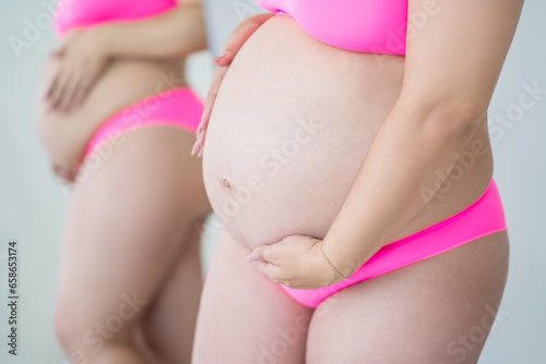 Pregnant woman in pink underwear on gray background, maternity underwear, pregnancy concept with reflection in the mirror