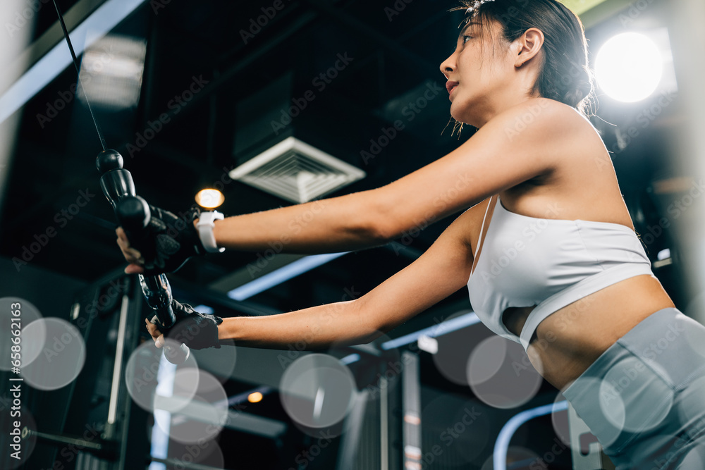 Beautiful woman working out indoors, using a pull-down weight machine to train her arms and build muscle. fitness center health workout concept
