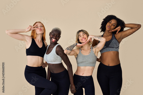 Happy fit sporty diverse different girls group having fun posing at beige background. Multiracial positive young women friends wear sportswear advertising fitness gym yoga body trainings together. © insta_photos