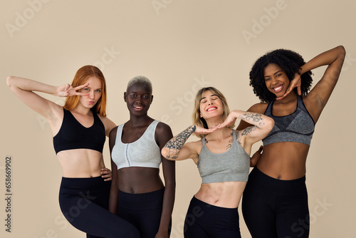 Happy fit sporty diverse different girls group having fun standing at beige background. Multicultural positive young women friends wear sportswear advertising fitness gym yoga body trainings together. © insta_photos