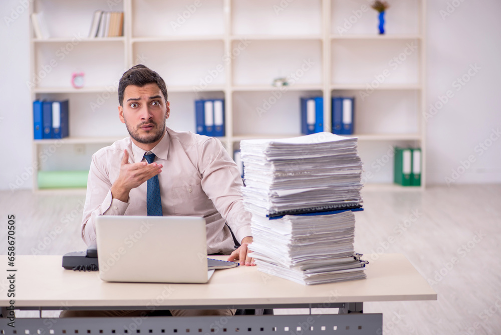 Young male employee unhappy with excessive work in the office Young male employee unhappy with excessive work in the office
