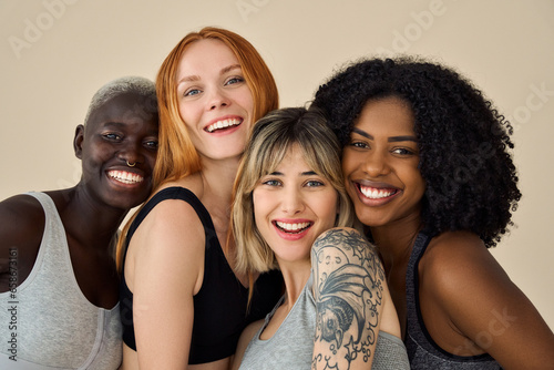 Smiling fit multi ethnic girls, four happy diverse young women models wearing sportswear tops bonding on beige background advertising natural beauty body care, group yoga fitness trainings. Portrait.